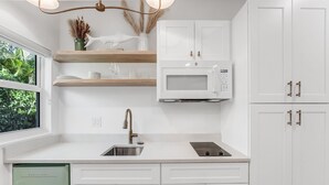 Una cocina moderna con armarios blancos, microondas integrado y ventana con vistas a la vegetación.