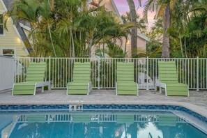 A pool area with green lounge chairs and a white fence, surrounded by palm trees. - Large King Bedroom in the heart of Sanibel (Sanibel)