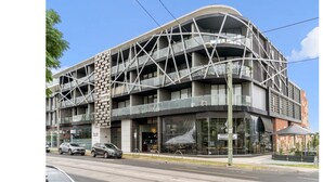 Un bâtiment moderne à plusieurs étages, doté d’une façade géométrique remarquable, d’un restaurant bien visible avec une terrasse, et surplombant un ciel dégagé.