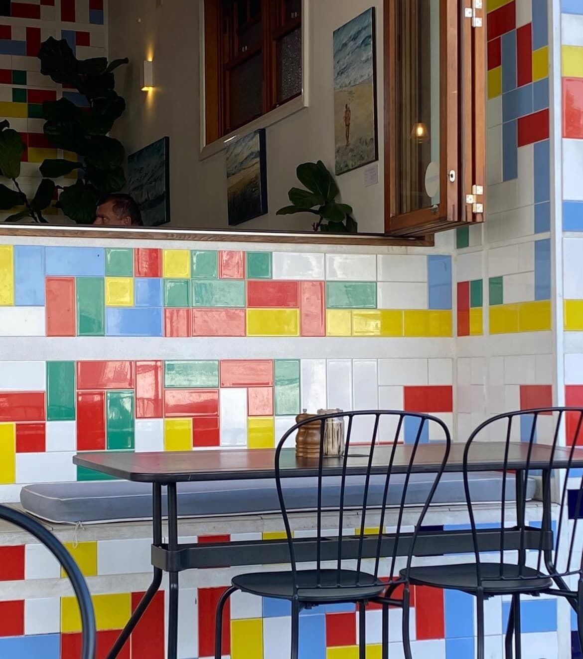 Ein Restaurantinneres mit farbenfrohen Fliesenwänden, einer Holztheke und schwarzen Metallstühlen.