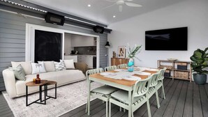 A modern outdoor living space with a dining table, chairs, a sofa, and a TV mounted on the wall. - Carrington Cottage | Walk to Cafés, Bars & Harbour (Carrington)