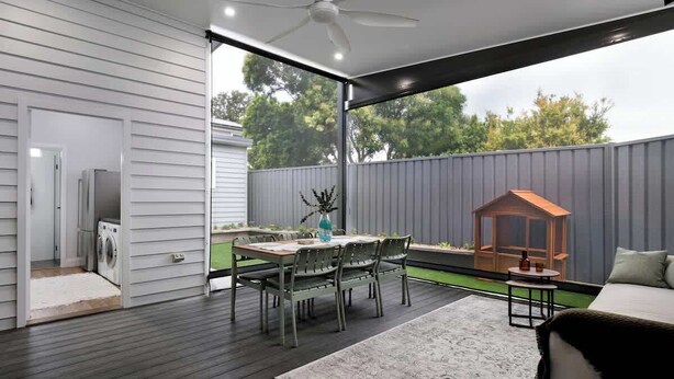A modern outdoor patio with a dining table and chairs, a ceiling fan, and a small playhouse. - Carrington Cottage | Walk to Cafés, Bars & Harbour (Carrington)