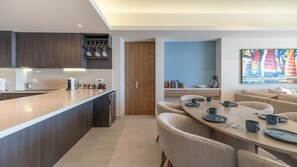 A modern kitchen with dark wood cabinets, a marble countertop, and a dining area with a light-colored table and chairs. - One 1706- Penthouse - State-of-the-Art Beachfront Escape Along the Sea of Cortez (Puerto Peñasco)