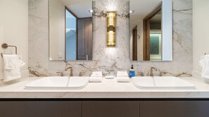 Ein modernes Badezimmer mit zwei Waschbecken, einem großen Spiegel und einer zentralen Leuchte.