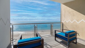 Een balkon met twee blauwe fauteuils, een glazen balustrade en uitzicht op het strand en de zee.