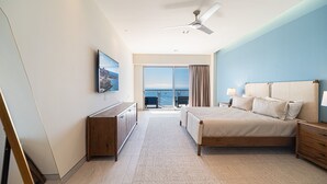 Een slaapkamer met een bed, nachtkastjes, een televisie en uitzicht op de oceaan door een schuifdeur.