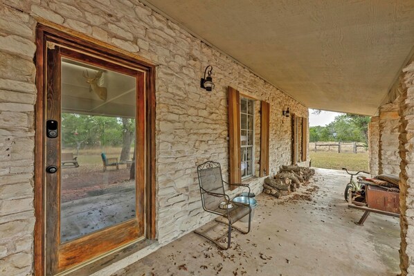 A covered porch with stone walls, wooden doors, and a metal chair. - Double H Ranch | Cozy 2-bedroom retreat + perfect for families! (Dripping Springs)