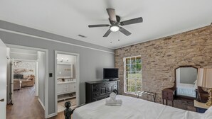 A bedroom with a bed, a dresser, a television, and a stone wall. - Double H Ranch | Cozy 2-bedroom retreat + perfect for families! (Dripping Springs)