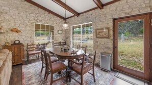 A stone-walled dining area with a wooden table and chairs, a chandelier, and a view of the outdoors. - Double H Ranch | Cozy 2-bedroom retreat + perfect for families! (Dripping Springs)