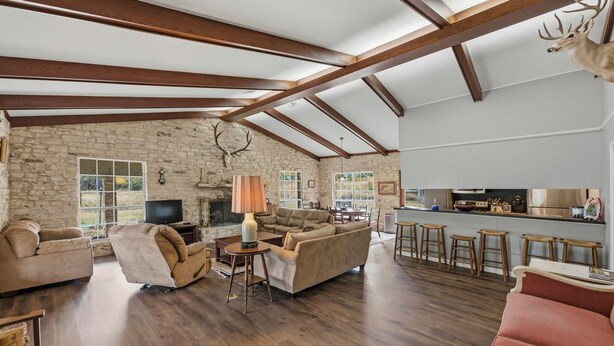 A spacious living room with a stone wall, wooden beams, a fireplace, and a kitchen area with stools. - Double H Ranch | Cozy 2-bedroom retreat + perfect for families! (Dripping Springs)