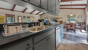 A kitchen with dark cabinets, a stone wall, and a dining area with wooden chairs and a table. - Double H Ranch | Cozy 2-bedroom retreat + perfect for families! (Dripping Springs)