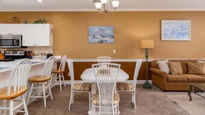 A dining area with a white table and chairs, a kitchen with white cabinets, a brown sofa, and two paintings on the wall. - Serene pool peaceful first floor kitchen washer dryer (Myrtle Beach)