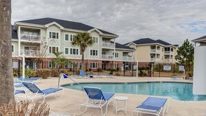 A pool area with lounge chairs and a building with multiple balconies. - Serene pool peaceful first floor kitchen washer dryer (Myrtle Beach)