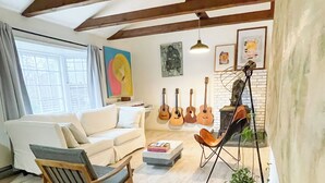En hyggelig stue med trægulv, en hvid sofa, en træstol og et sofabord. Der hænger guitarer på væggen, og der står en plante på et træstel.