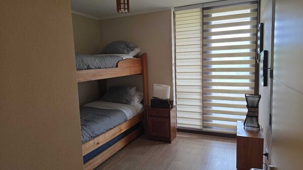 A room with a bunk bed, a desk with a lamp, and a window with blinds. - Departamento Costanera Playa (Villarrica)