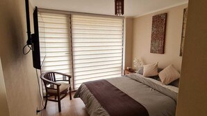 Ein Schlafzimmer mit einem Bett, einem Sessel, einem Nachttisch, einer Lampe und einer Heizung.