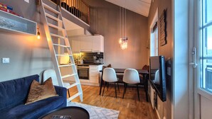 Ett kompakt bostadsutrymme med en soffa, en matplats, ett kök och en tv som är monterad på väggen.