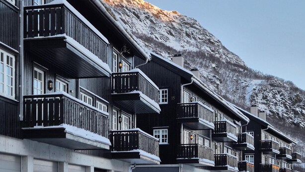 En rad trähus med balkonger, vart och ett numrerat, med ett snöklätt berg i bakgrunden.