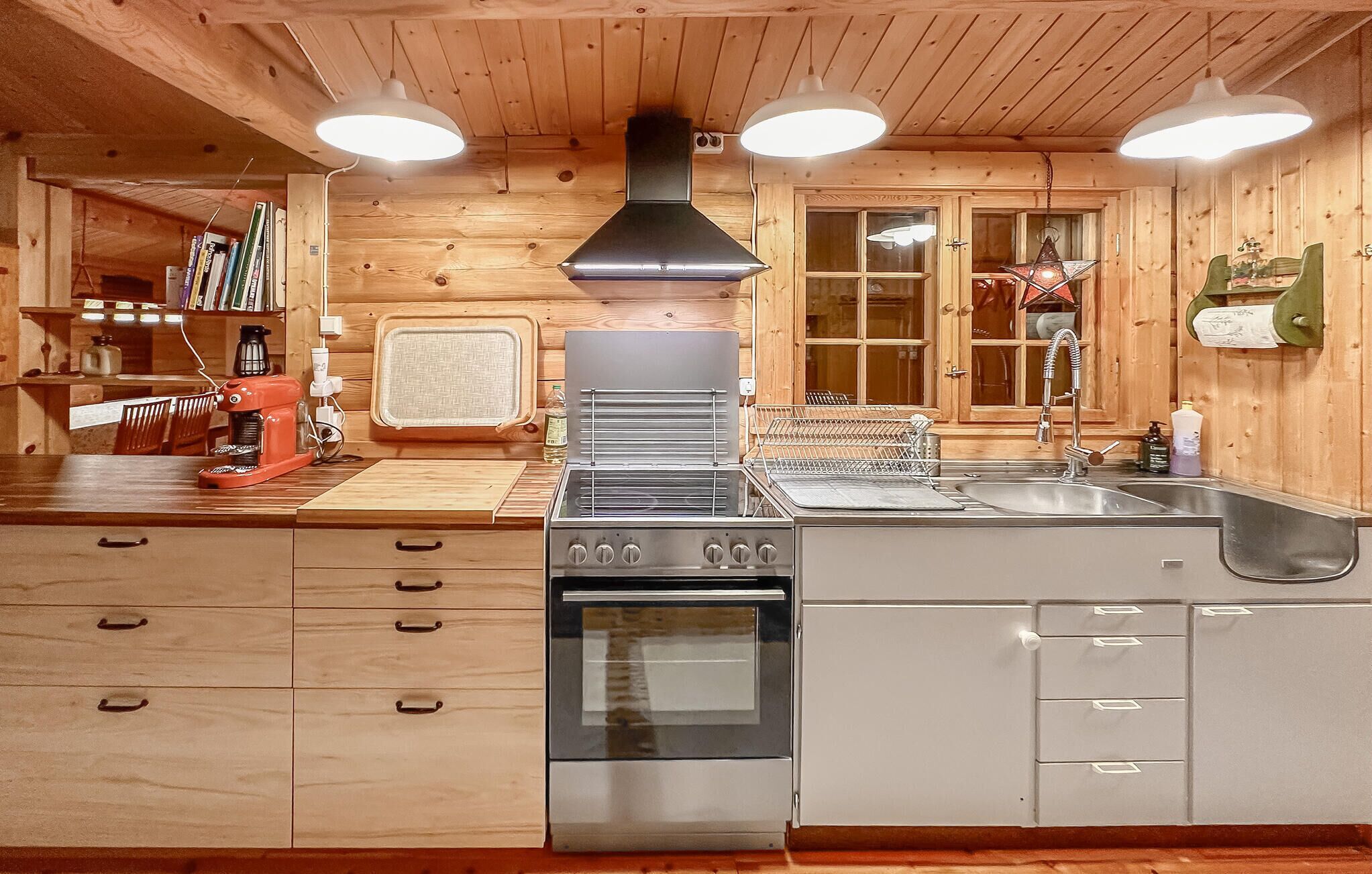 A modern kitchen with wooden walls, a stainless steel stove, a sink, and a window overlooking a scenic view.