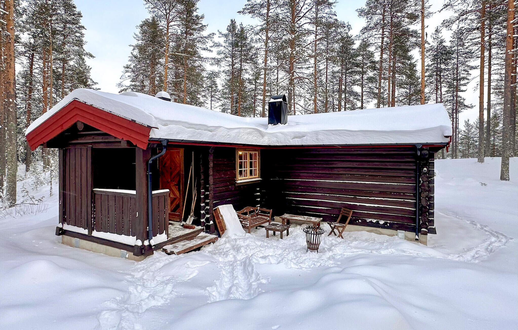 Una cabaña de madera con techo rojo y chimenea, rodeada de árboles cubiertos de nieve.