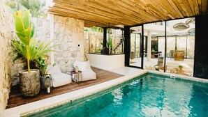 Ein moderner Poolbereich im Innenbereich mit Steinwänden, Holzböden und einer verglasten Terrasse.