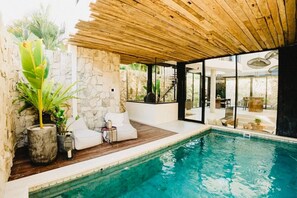 Ein moderner Poolbereich im Innenbereich mit Steinwänden, Holzböden und einer verglasten Terrasse.