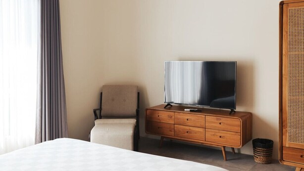 Ein Hotelzimmer mit einem Bett, einer Holzkommode mit Fernseher, einem Sessel und einem Korbtisch.
