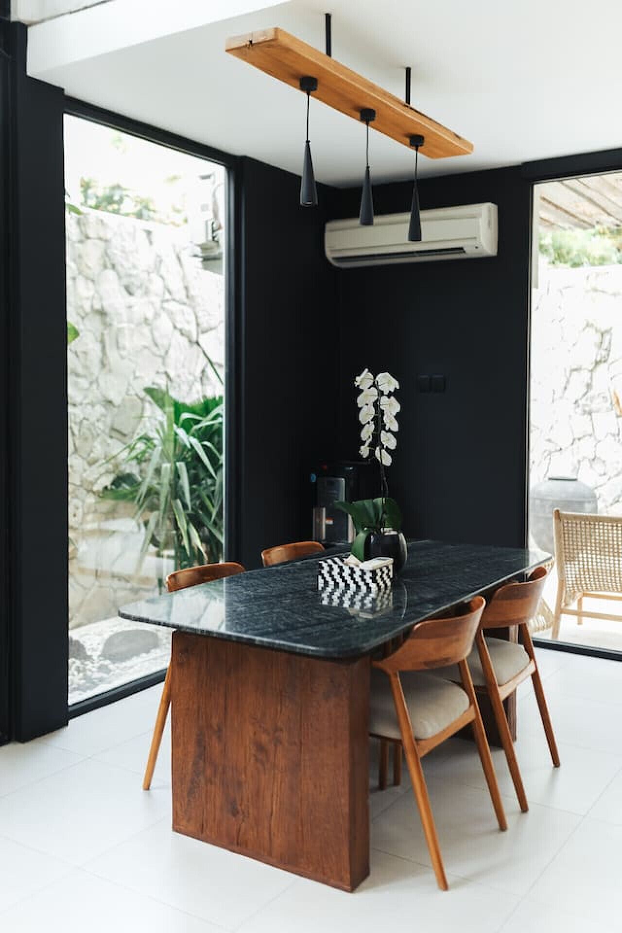 A dining area with a black marble table, wooden chairs, a hanging light fixture, and a potted plant.