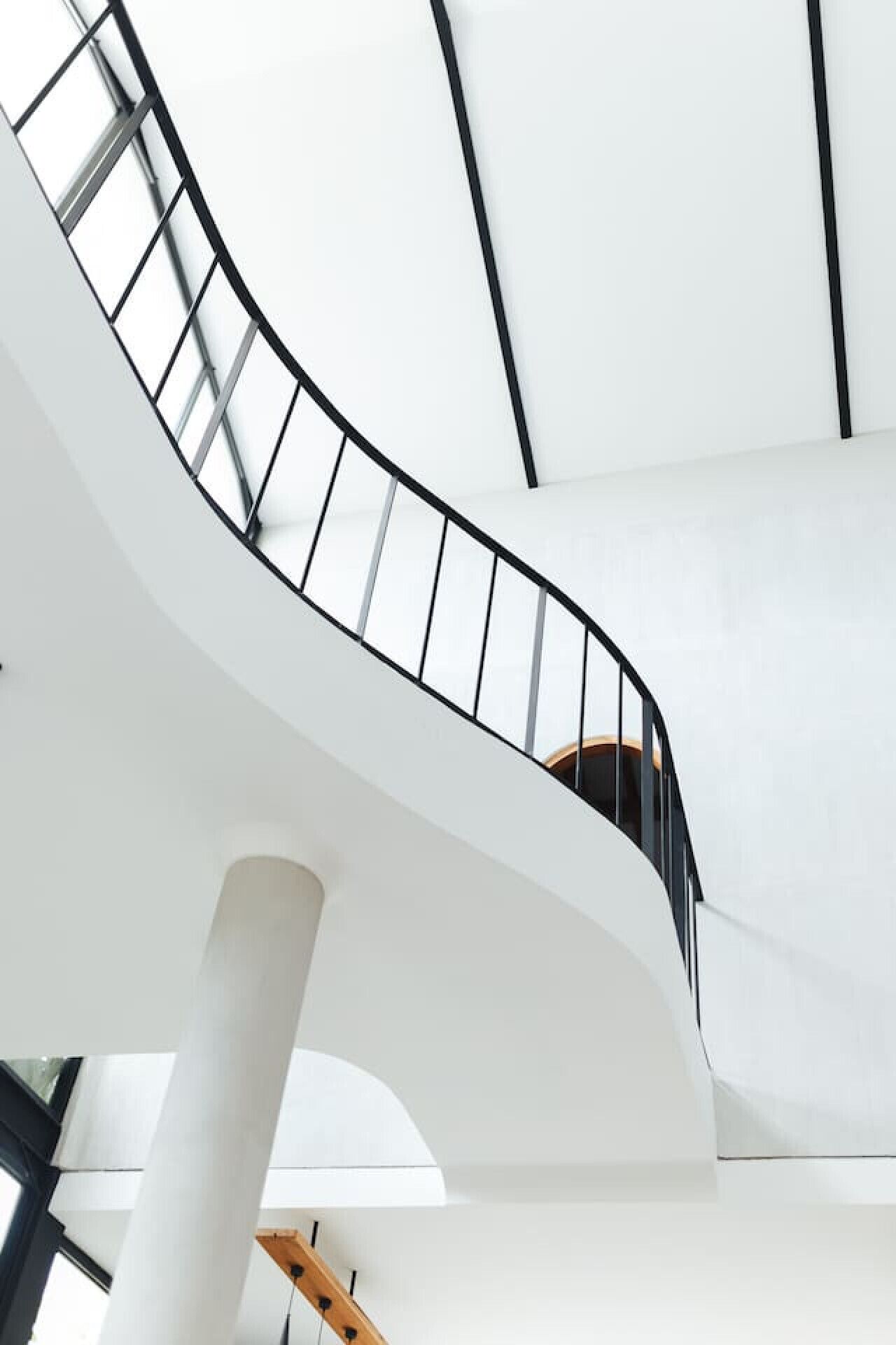 A spiral staircase with a black railing, white walls, and a wooden handrail.