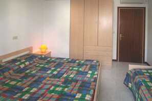 Een slaapkamer met twee bedden, een kledingkast, een nachtkastje met lamp en een deur.
