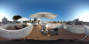 Una terraza en la azotea con una cerca blanca, una mesa con sillas y un paraguas grande.