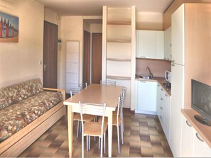Ein gemütlicher Wohnbereich mit Sofa, Esstisch, Stühlen, einer Küchenzeile mit Schränken und einer Mikrowelle sowie einem Fernseher.
