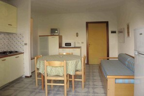 A compact kitchen with a dining table, chairs, a microwave, and a small refrigerator. - Holiday apartment mit Klimaanlage und Balkon (Lignano Sabbiadoro)