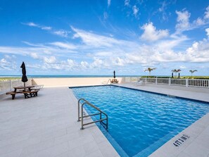 Ein Swimmingpool mit weißer Liegefläche, einem Picknicktisch und Liegestühlen.