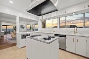 A modern kitchen with a central island, built-in appliances, and large windows offering a view. - Prestigious Hills Estate | Stunning Pool & Hot Tub Views (San Diego)