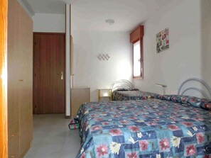 Ein Schlafzimmer mit einem großen Bett, einem kleineren Bett, einem Kleiderschrank, einem Schreibtisch und einem Fenster mit Blick nach draußen.