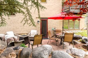 Une terrasse extérieure avec des meubles en osier, un parasol rouge et un mur en pierre.