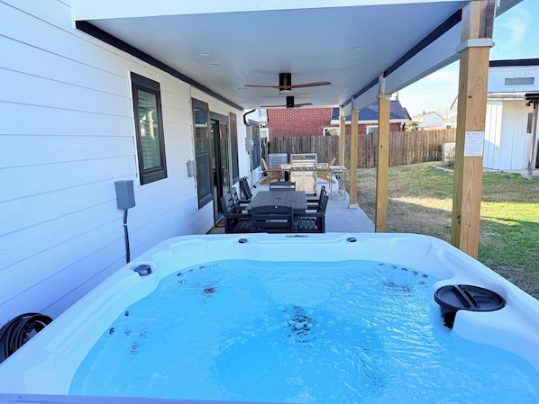 Een achtertuin met een jacuzzi, een overdekt terras en een barbecueplek.