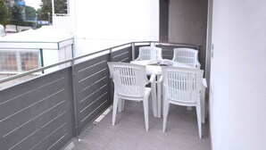 Uma varanda com mesa e quatro cadeiras brancas, grades cinzentas e piso de azulejos.
