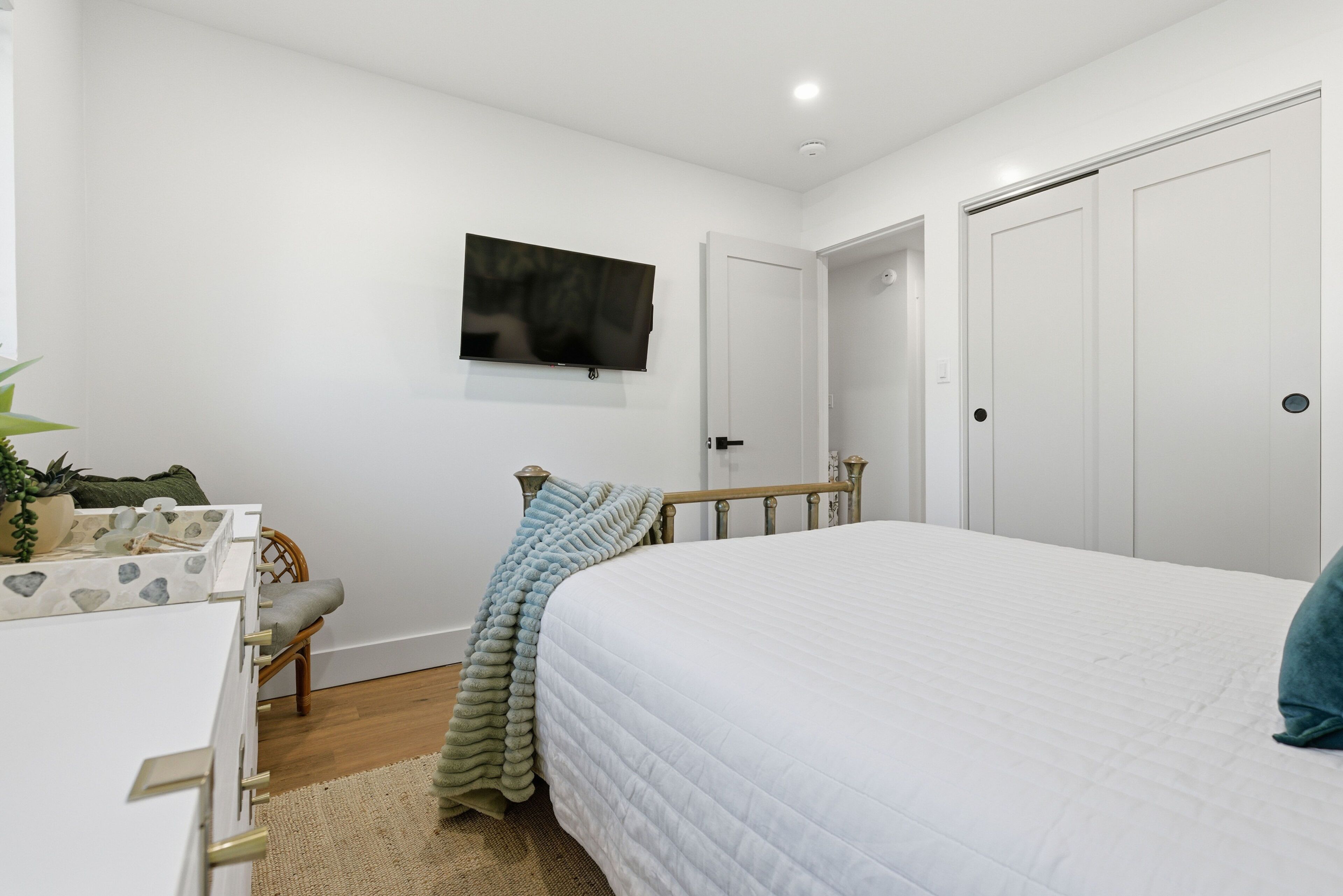 A bedroom with a bed, a television mounted on the wall, a door, and a small seating area with a chair and a table.