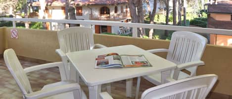 Une terrasse avec une table et des chaises, un magazine posé sur la table, et une vue sur des maisons et des arbres en arrière-plan.