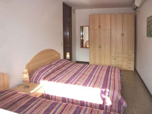 A bedroom with a bed, a nightstand, a lamp, a wardrobe, and a mirror. - Holiday apartment mit Klimaanlage und Balkon (Lignano Sabbiadoro)