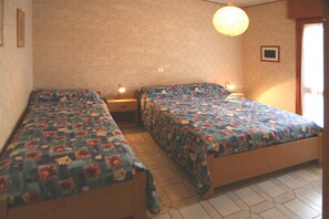 Quarto com duas camas de solteiro, cada uma com colcha de padrão floral e mesa de cabeceira com abajur.