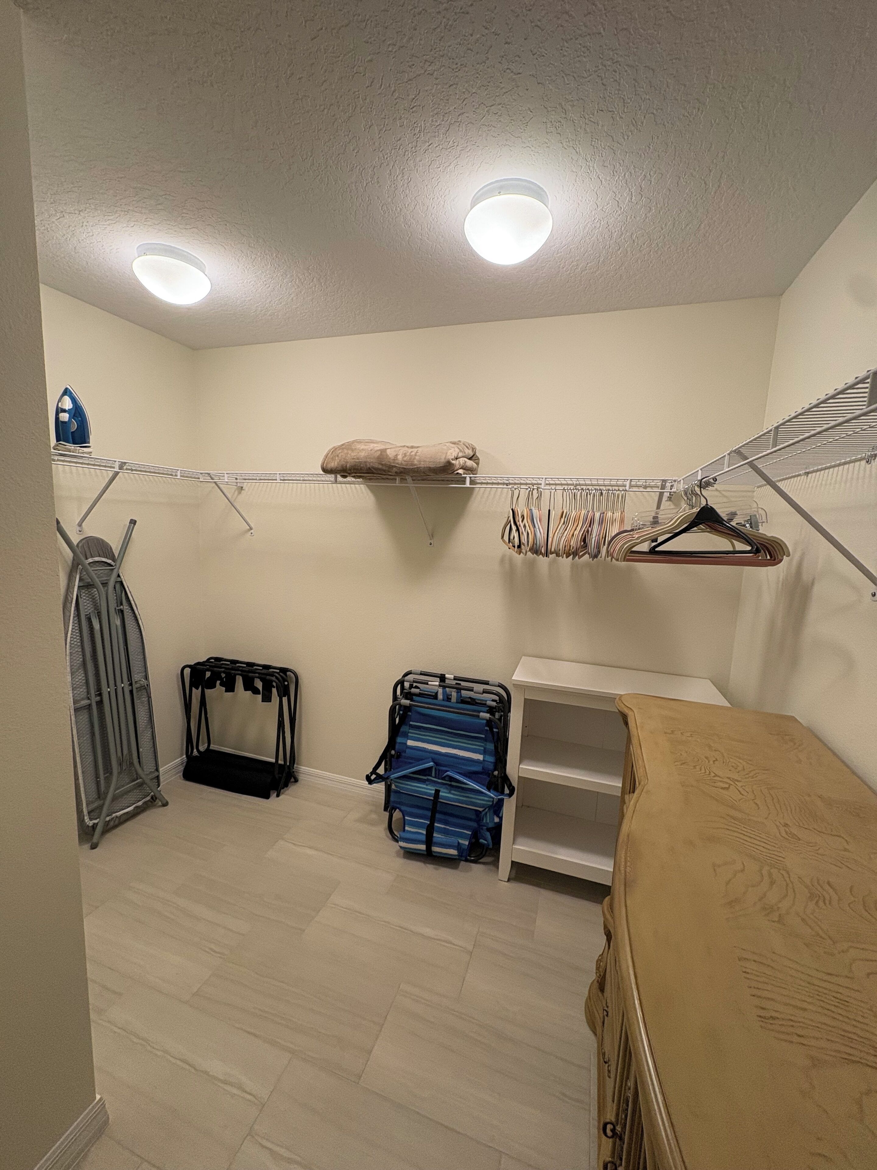 A laundry room with a drying rack, ironing board, and a shelf with folded clothes.