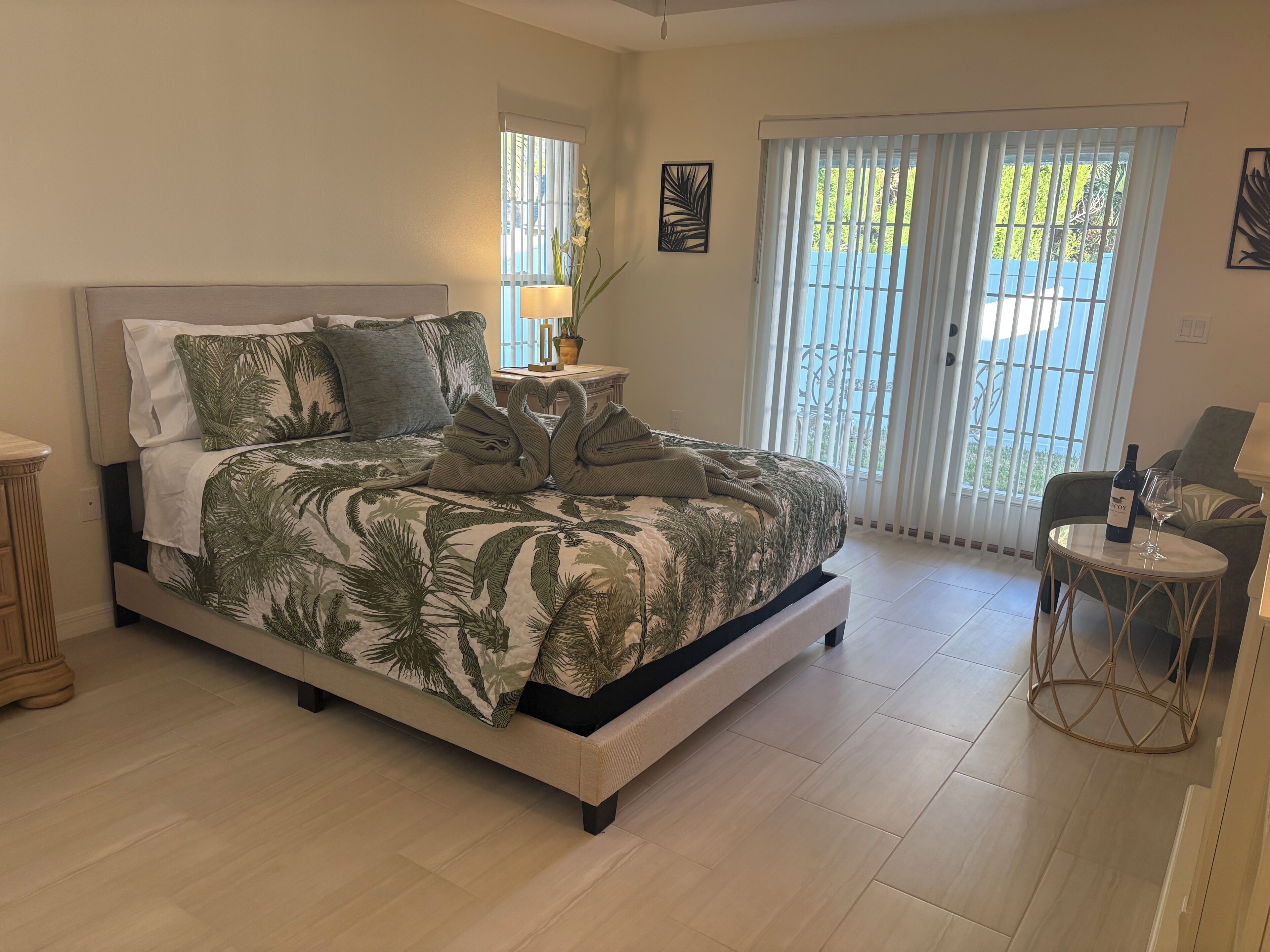 Une chambre à coucher comprenant un lit, une table de chevet, une lampe, une chaise et une fenêtre avec des stores.