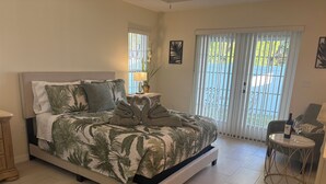 Ein Schlafzimmer mit Bett, Nachttisch, Lampe, Stuhl und Fenster mit Jalousien.