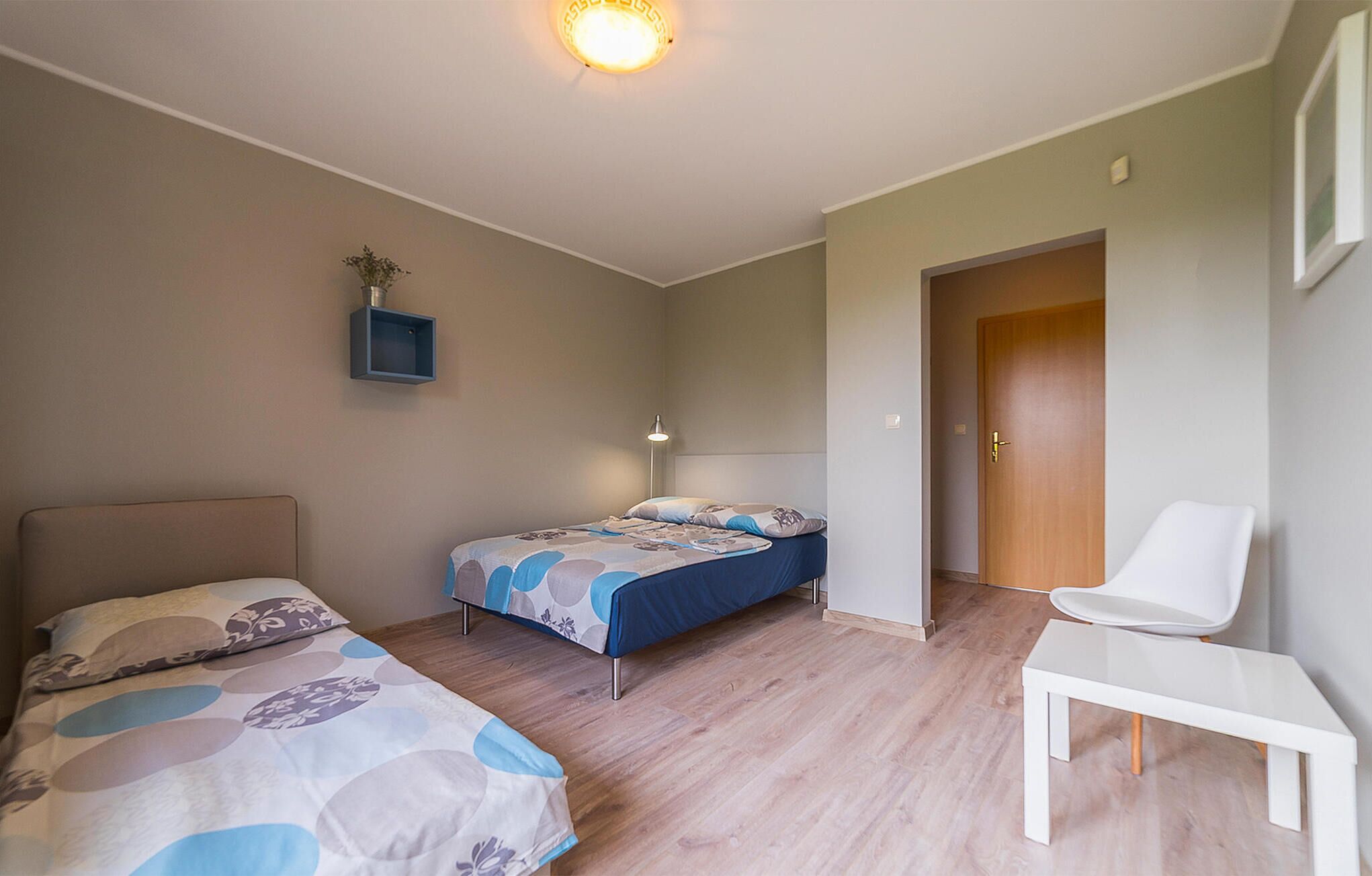 A bedroom with two beds, a desk, and a chair. There is a door leading to another room.