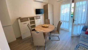 Un comedor con una mesa redonda, sillas, un televisor y un puerta corrediza de vidrio que da a un área exterior.