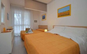 A hotel room with two beds, a desk, and a window with curtains. - Holiday apartment with air conditioning and balcony (Bibione)