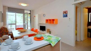Moderni keittiö, jossa on ruokailutila, suuri ikkuna, televisio ja oranssit hyllyt.